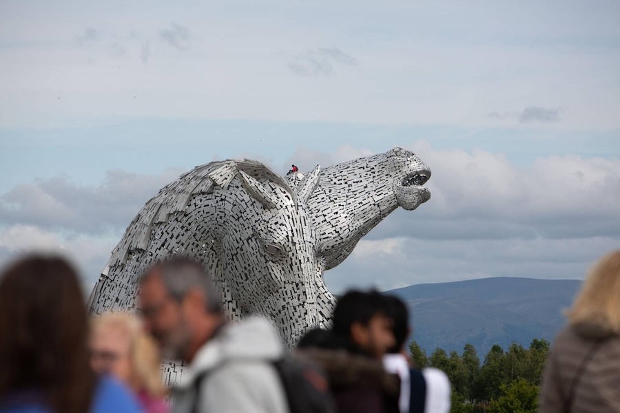 Photograph: the climbers sit on a kelpie's head. A crowd can be seen in soft focus in the foreground.